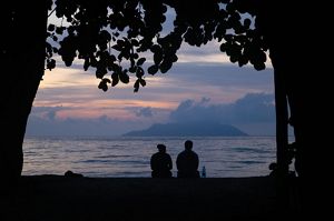 Dos personas silueteadas contra un cielo de atardecer en una playa. El cielo muestra colores púrpuras y rosados.