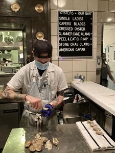 A restaurant worker shucking an oyster at the raw bar.