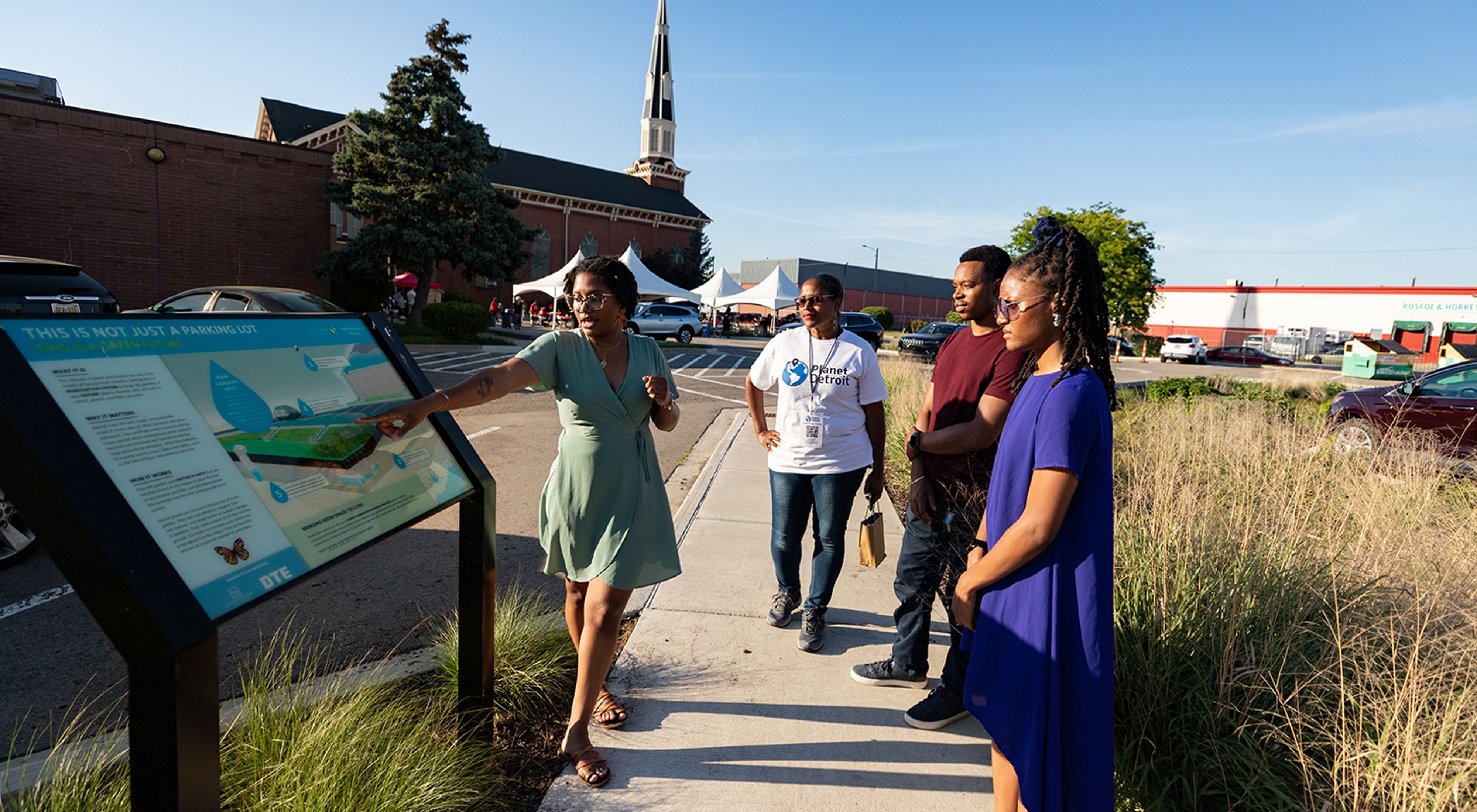 A group of people look at an informative sign on a sunny day at Sacred Heart Church in Detroit, Michigan. 