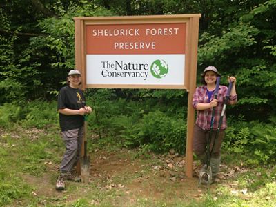 Two people standing in front of a sign that says Sheldrick Forest Preserve.