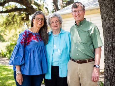 Two women and a man pose together in front of a house.