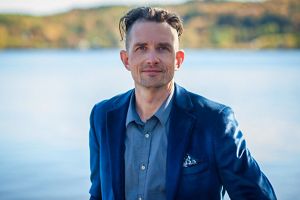 Man standing in front of nature smiling.
