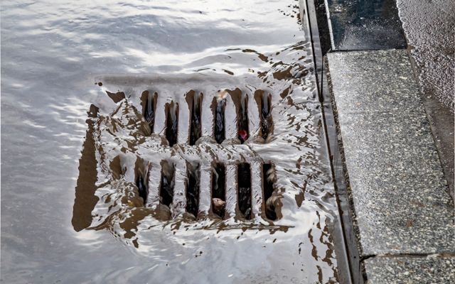 A sidewalk next to a catch basin with water flowing into the basin.