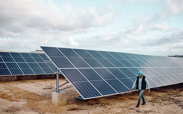 A man wearing a hardhat walks past solar panels.