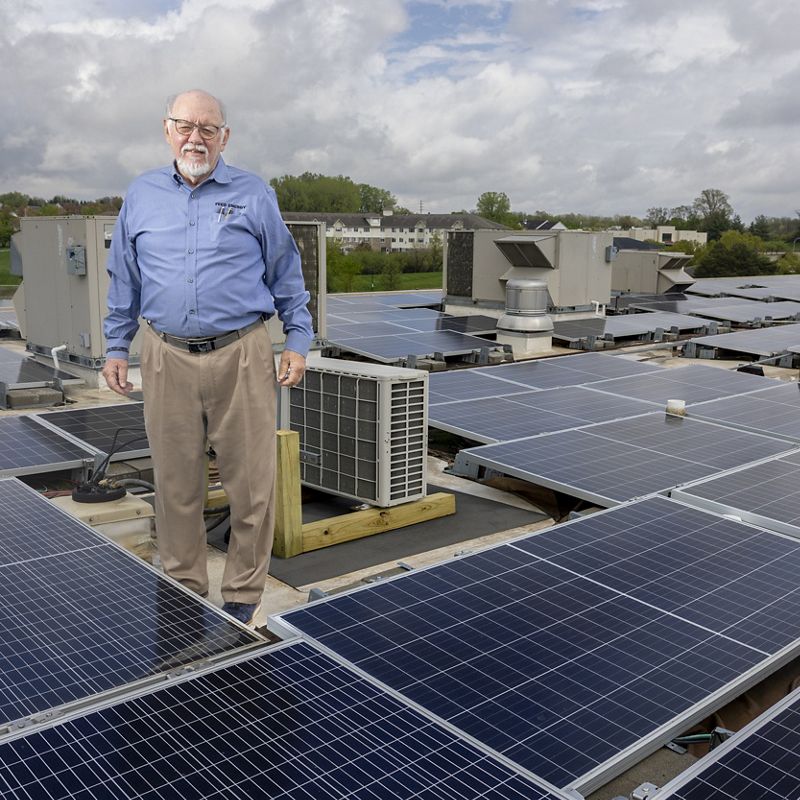 Bob Riley stands on solar-panel-covered roof.