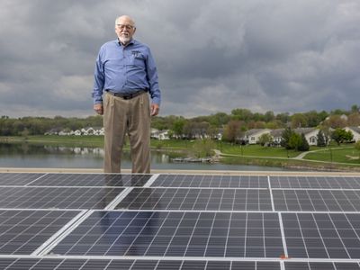 Bob Riley stands on a roof covered in solar panels.
