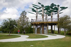 A curving walkway leads to the elevated platform of the Bird's Nest Learning Pavillion. Giant metal leaves shade the round structure.