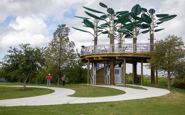 A curving walkway leads to the elevated platform of the Bird's Nest Learning Pavillion. Giant metal leaves shade the round structure.