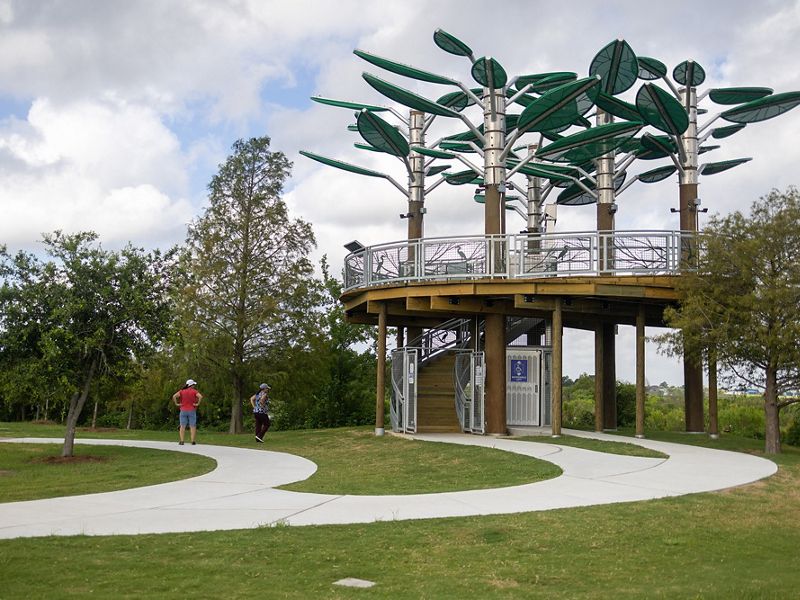 A curving walkway leads to the elevated platform of the Bird's Nest Learning Pavillion. Giant metal leaves shade the round structure.