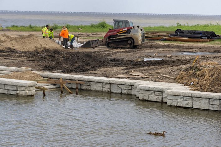 A group of men work near a small bulldozer at a construction site along a river.