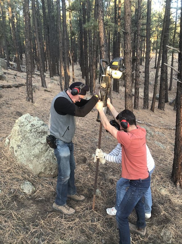 Three people situate a stake into a hole in the ground.