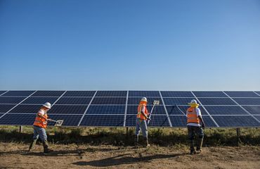 Three workers use long handled tools to clean the surface of a solar panel array.