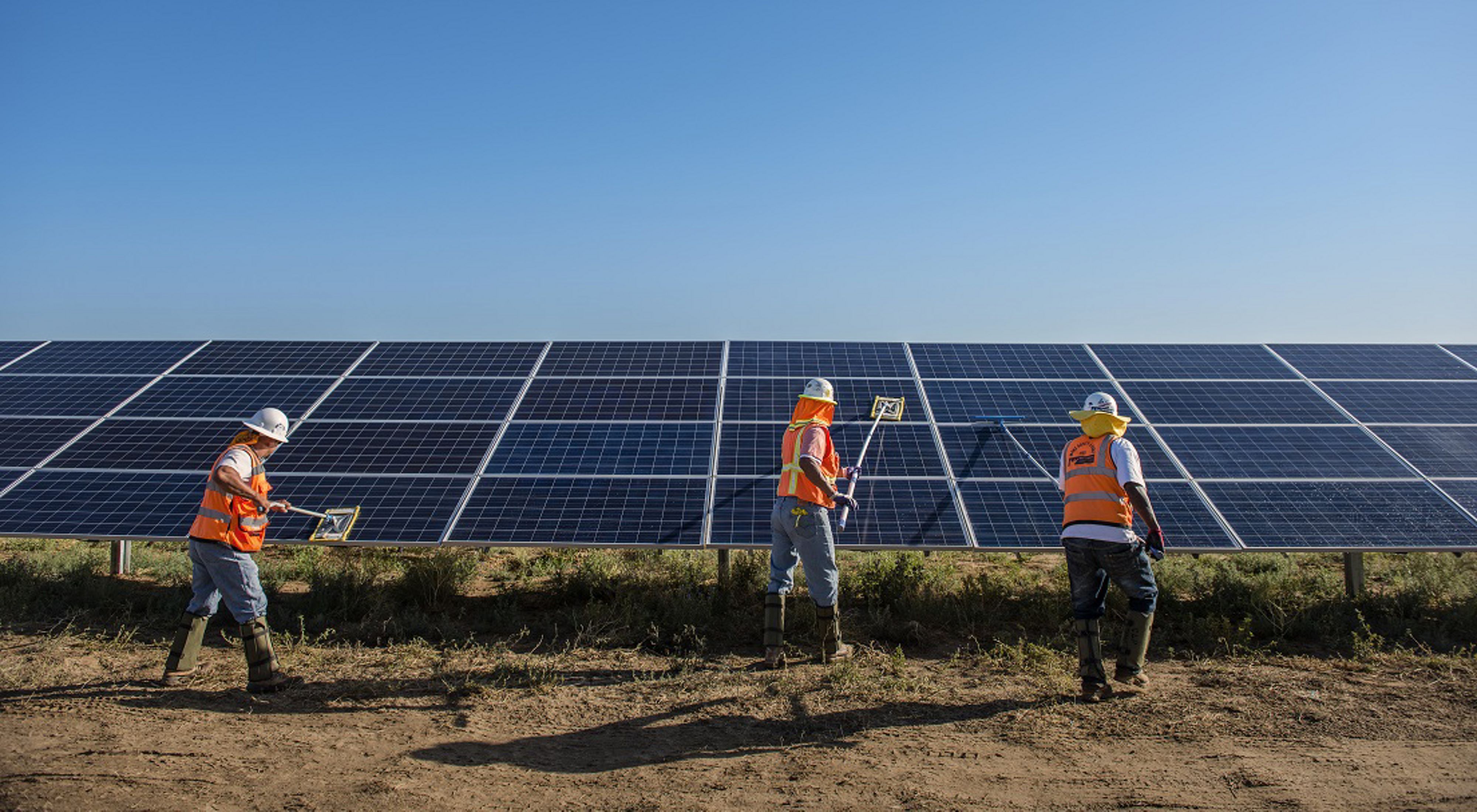Three workers in hard hats cleaning solar panels