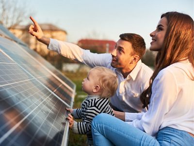 A man, woman and child look at a solar panel.