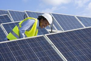 A woman wearing a hard hat and safety vest inspects solar panels.