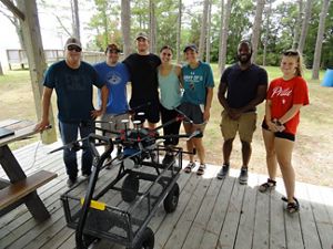 A group of seven college students pose around a drone. 