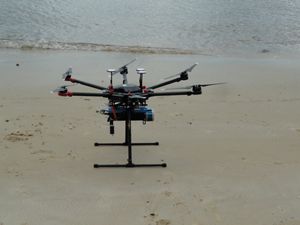 A drone is situated in sand next to water.