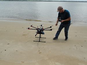 A man stands next to a drone on a beach.