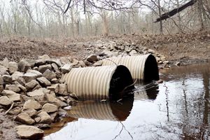 Big culverts with stagnant water going through them. Rocks and debris are surrounding the space.