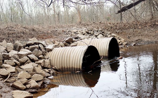 Big culverts with stagnant water going through them. Rocks and debris are surrounding the space.
