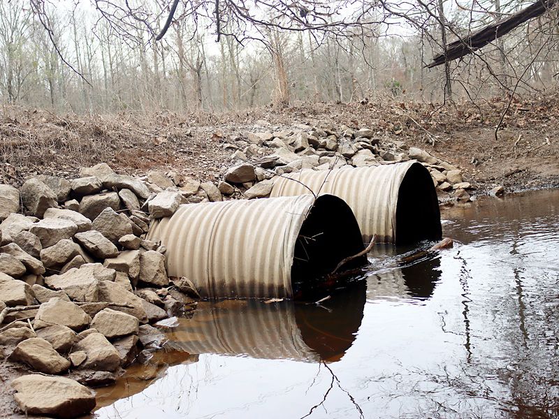 Big culverts with stagnant water going through them. Rocks and debris are surrounding the space.