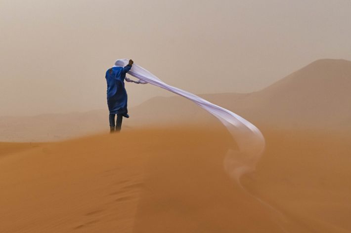 Un guía en el desierto del Sahara durante una tormenta de arena. La larga envoltura de la cabeza de la persona, desenredada, golpea hacia un lado en la arena.