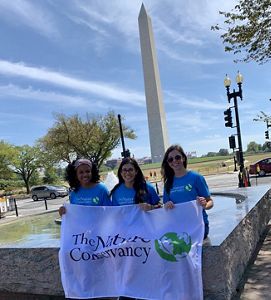 Three TNC employees holding the TNC flag in Washington D.C., with the Washington Monument in the background.