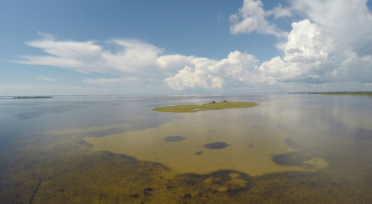 View of bay with green and blue water under a blue cloudy sky.