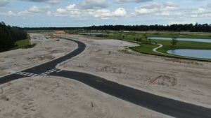 A golf course and newly cleared land make way for a winding asphalt road. 