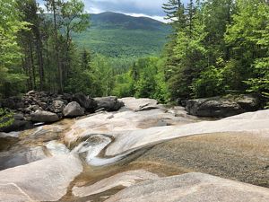 A view looking down the rocky slope of a waterfall with mountains beyond.