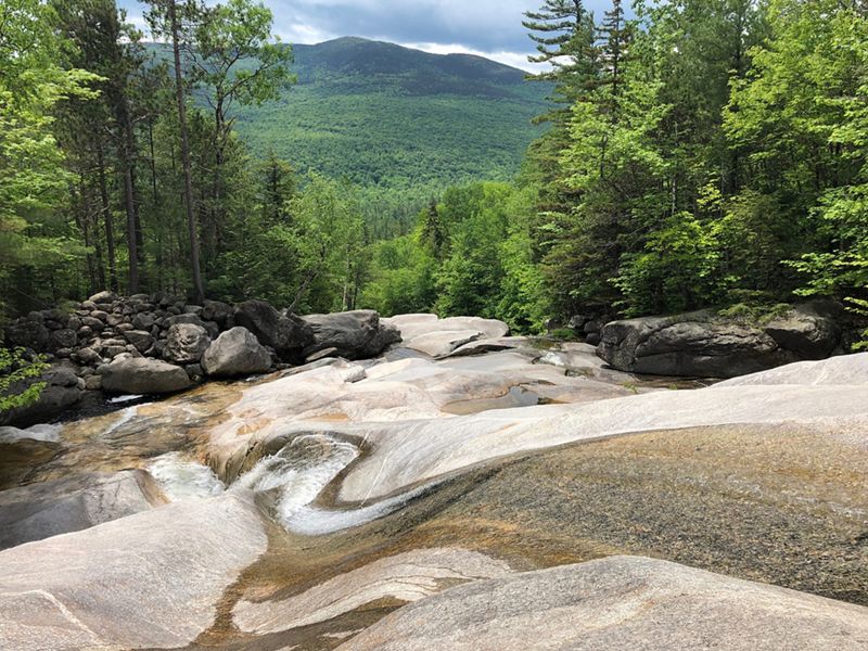 A view looking down the rocky slope of a waterfall with mountains beyond.