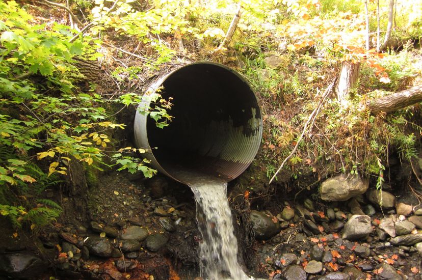 Water flows out of a large metal pipe into a puddle. 