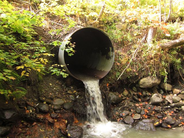 Water flows out of a large metal pipe into a puddle. 