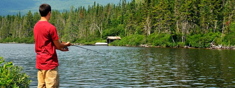 A man in a red shirt fishing in a lake.