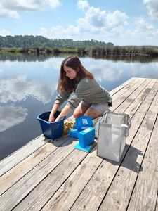 a women in her knees on a boat deck putting both of her hands in a bucket.