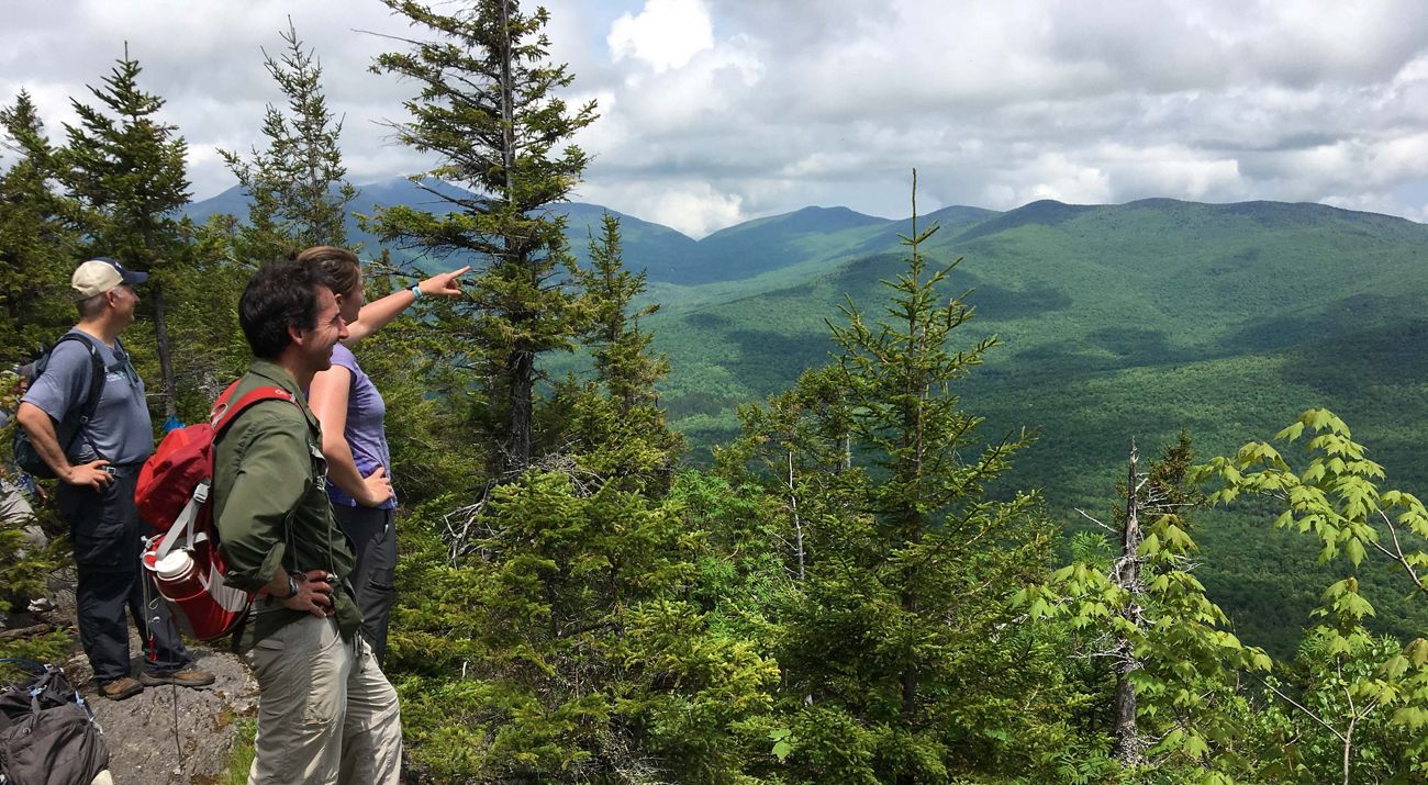Three people standing on Burnt Mountain in Vermont, looking at the view.