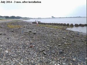 Rocky, barren shoreline with a row of reef balls and water in the background.