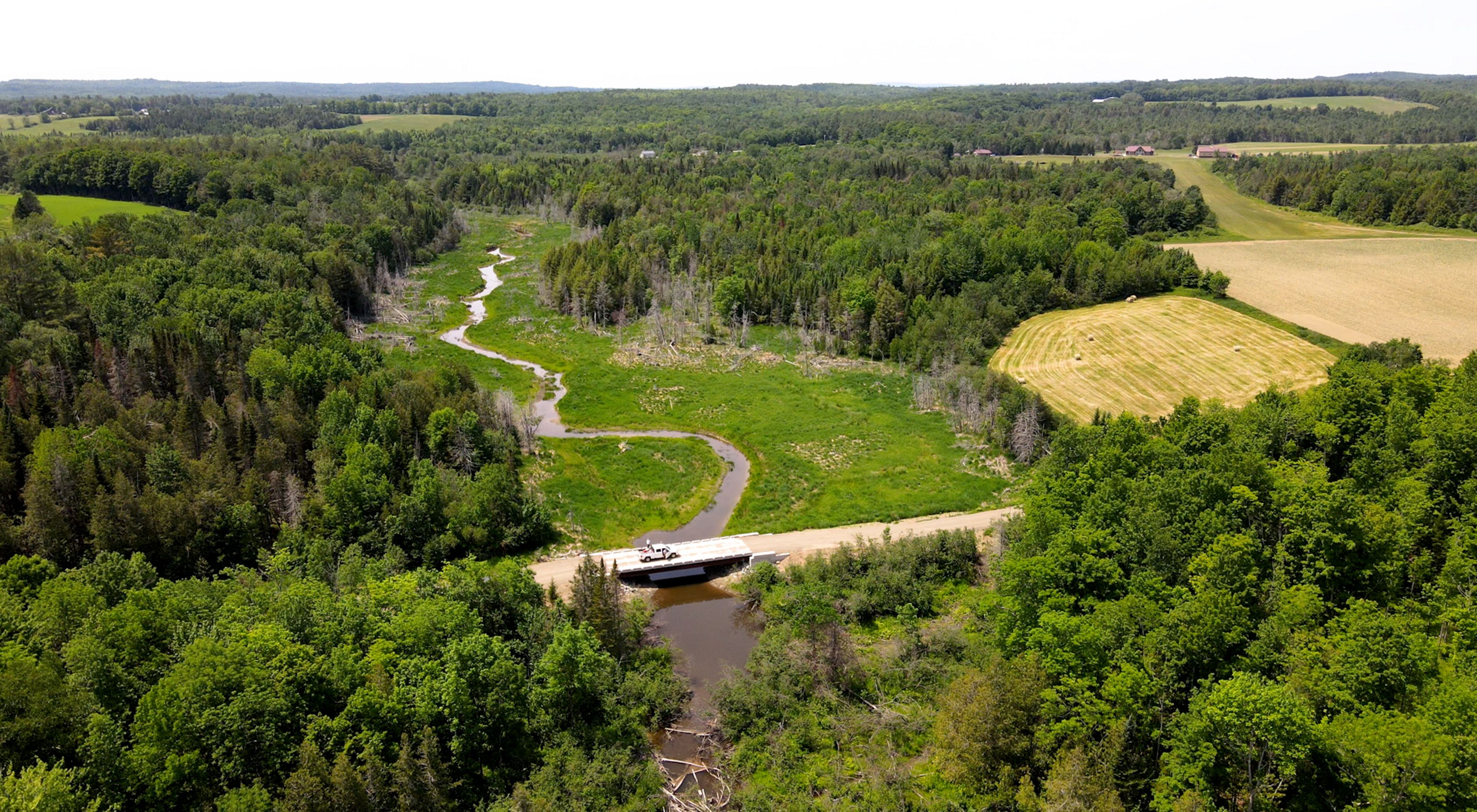 Aerial view of a truck parked on a bridge over a stream.