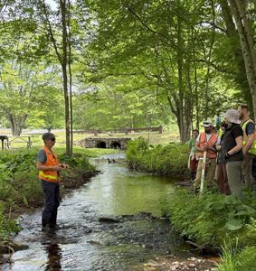 A group of people gather around a narrow, brown stream.