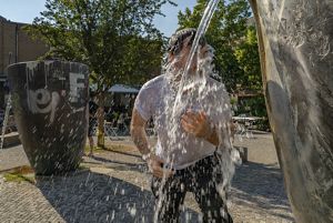 man stands with face splashed by water in a plaza