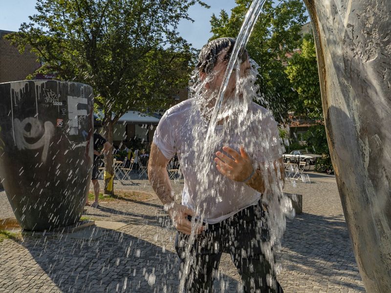 man stands with face splashed by water in a plaza