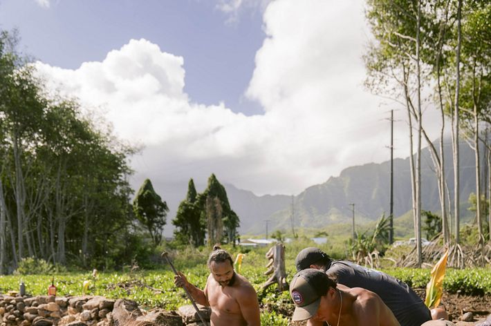 Workers in black loincloths stack stones in a wall.
