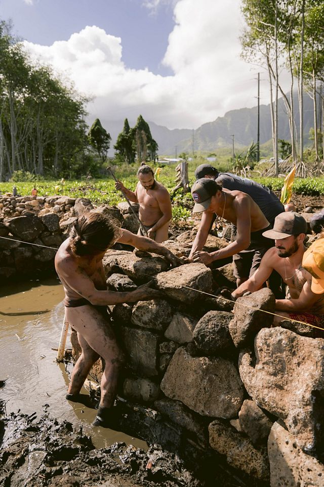Workers in black loincloths stack stones in a wall.
