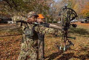 Two men both wearing camo line up arrows on their compound bows. 