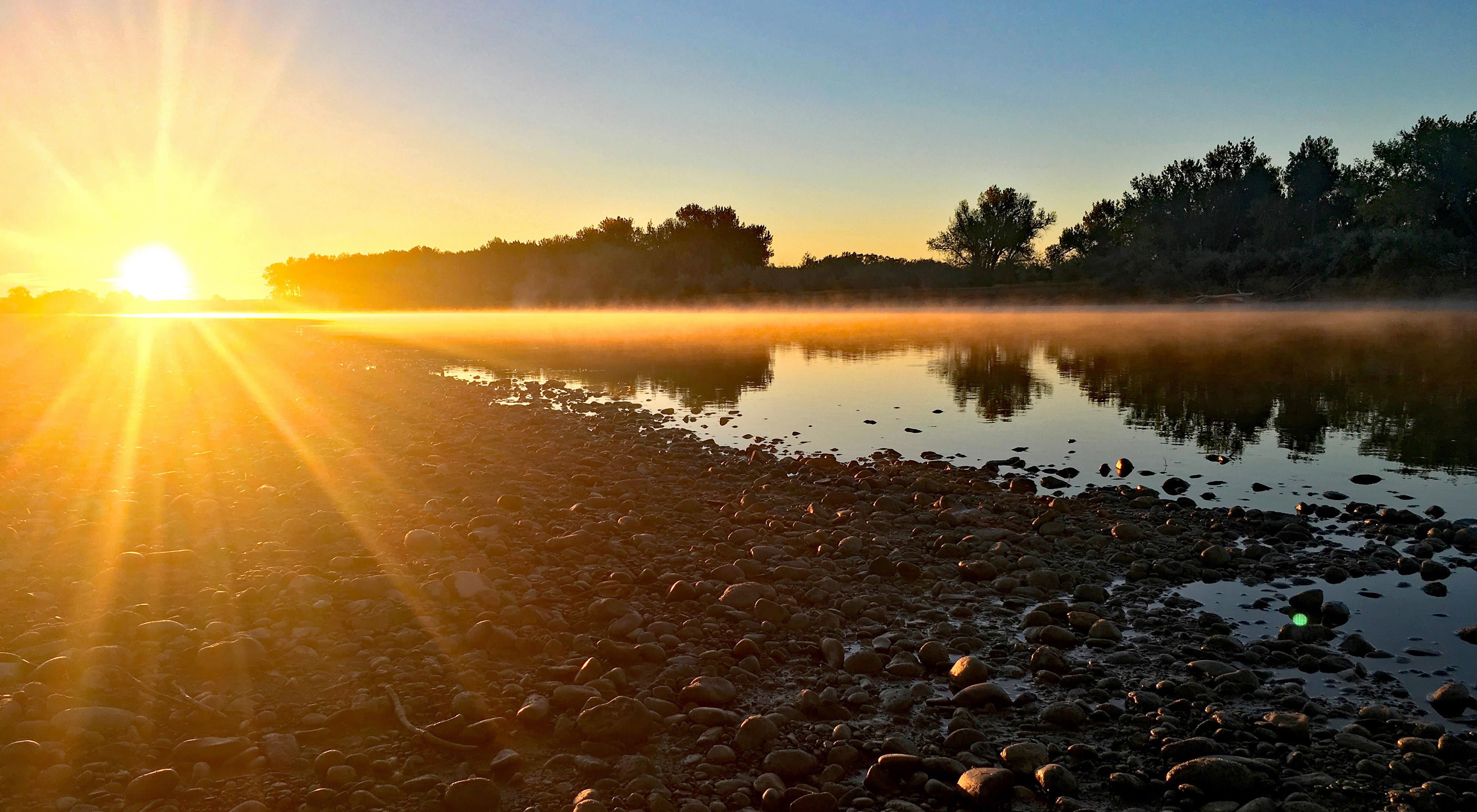 Sun rising over the Yellowstone River with views of the river and surrounding treeline.