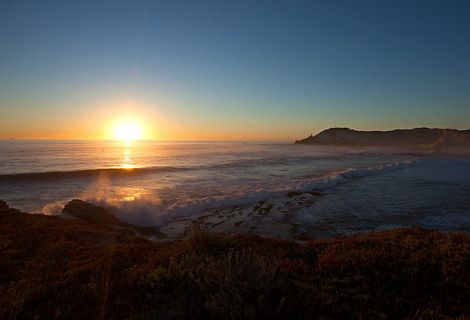 Sun sets over the ocean with gentle waves lapping up against the shore, viewed from a beach.