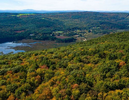 A view of fall trees on a mountain top looking over a river with more mountains in the distance.