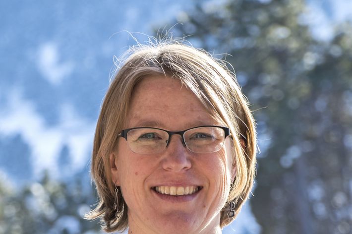 Headshot of Coastal Science Program Manager Susan Bates. A smiling woman wearing a navy blue cardigan stands in front of a blue sky and a tree with green leaves.