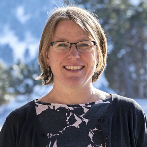 Headshot of Coastal Science Program Manager Susan Bates. A smiling woman wearing a navy blue cardigan stands in front of a blue sky and a tree with green leaves.