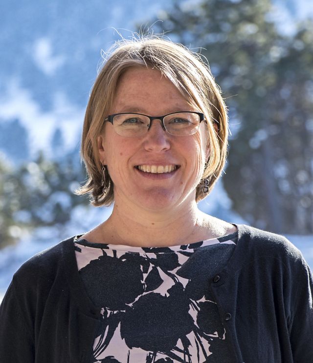 Headshot of Coastal Science Program Manager Susan Bates. A smiling woman wearing a navy blue cardigan stands in front of a blue sky and a tree with green leaves.